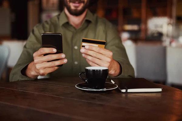 Крупним планом веселий щасливий кавказький чоловік рука тримає мобільний телефон набираючи реквізити картки, щоб зробити онлайн оплату сидячи в кафе — стокове фото