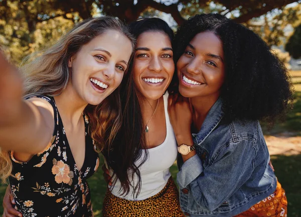 Autorretrato de cerca de jóvenes sonrientes amigas multiétnicas tomando selfie en el parque - mujeres tomando un selfie en el parque en un día brillante — Foto de Stock