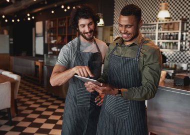 Cheerful cafe partners wearing apron standing inside a coffee shop looking on their touchscreen