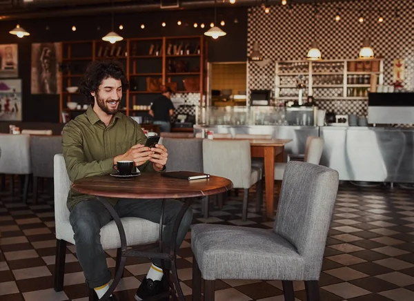 Щасливий білий молодий чоловік сидить у кафе, використовуючи мобільний телефон — стокове фото