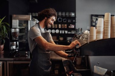 Smiling man with apron preparing coffee for customer in his small business