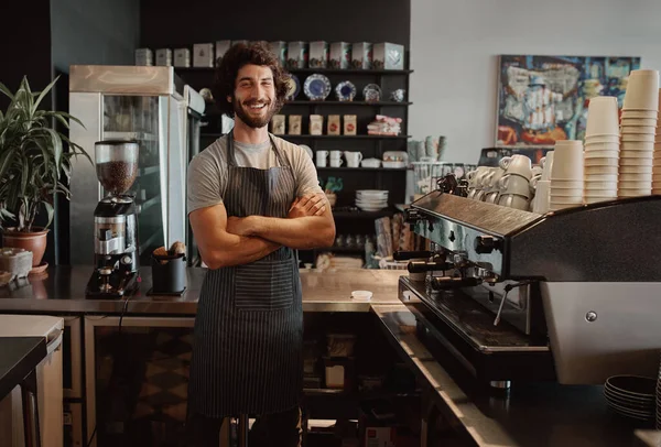 Successful male business owner behind the counter of a coffee shop with folded hands smiling looking at camera — Stockfoto