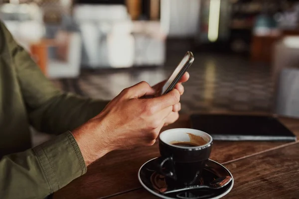 Primer plano de las manos del hombre usando el teléfono inteligente mientras está sentado en la cafetería bebiendo café — Foto de Stock