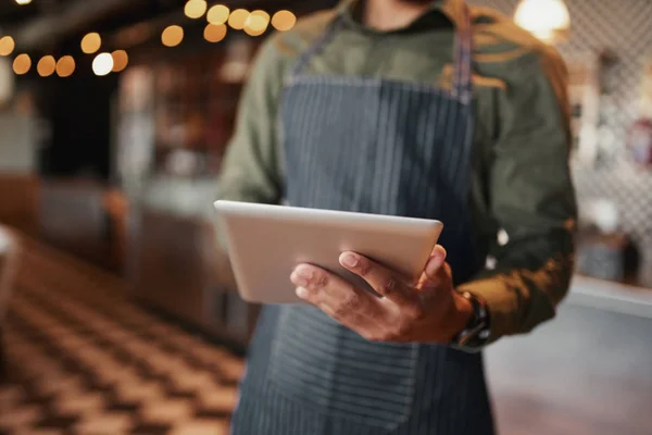 Primo piano del giovane cameriere che indossa il grembiule con tablet digitale in piedi in caffetteria — Foto Stock