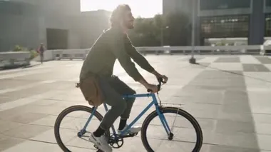 Happy young man with his bag riding bicycle in city street on sunny day