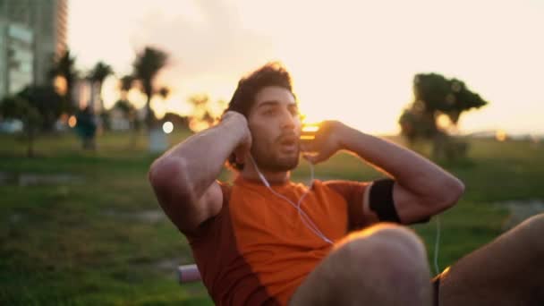 Fit young man training abs muscles sit-up crunches bodyweight floor exercises at park — Stok video