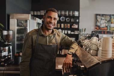 Portrait of young afro-american male business owner behind the counter of a coffee shop smiling looking at camera