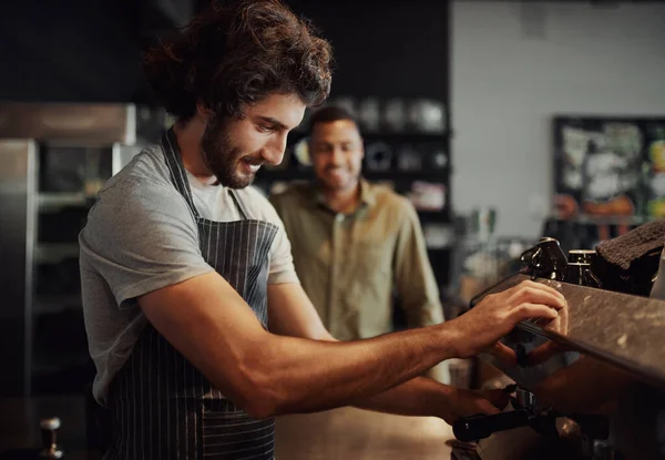 Handsome successful male worker making fresh coffee using machine while customer watching through counter — Stock Photo, Image