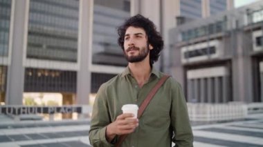 Portrait of smiling young businessman standing outdoors in front of a modern office courtyard holding takeaway coffee cup