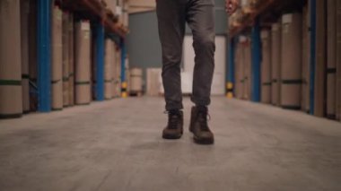 Büyük depo dağıtım merkezinde kameraya doğru yürüyen bir müdürün alt kısmı.