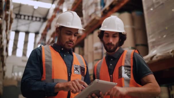 Divers jeunes travailleurs masculins discutent et utilisent une tablette numérique tout en supervisant la production à l'entrepôt de distribution — Video