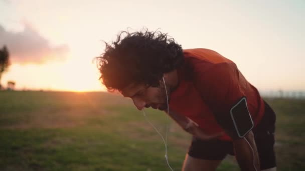 Joven guapo que parece cansado de correr al aire libre y tomar un descanso para tomar un poco de aire — Vídeos de Stock