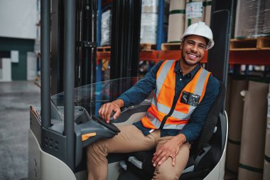 Depoda kameraya bakarken güvenlik yeleği ve beyaz kasketli mutlu bir Afrikalı forklift yöneticisinin portresi bir raftan diğerine mal taşıyor.