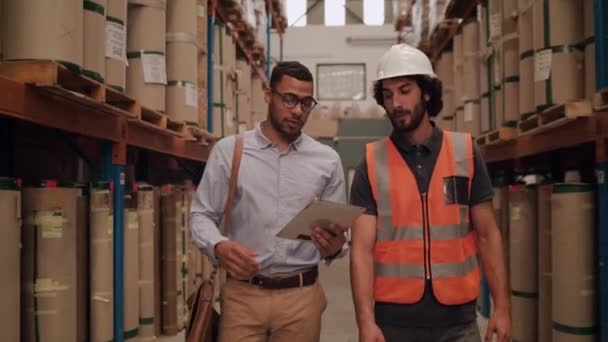 Deux employés marchent avec un ordinateur tablette à l'entrepôt du centre logistique ayant la discussion et serrent la main après avoir fait un marché — Video