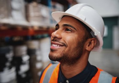 Side close-up of successful african american male worker looking away in warehouse wearing a white helmet