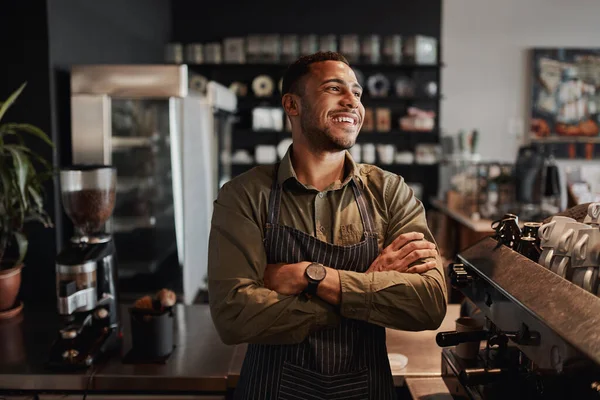 Young afro-american small coffee shop owner standing behind counter wearing apron with crossed arms looking away — Stock Photo, Image