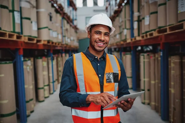 Happy male factory manager using digital tablet in warehouse while standing against goods shelf looking at camera — Stockfoto