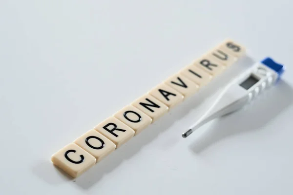 Coronavírus espelhado com telhas scrabble e termômetro em um fundo branco liso — Fotografia de Stock