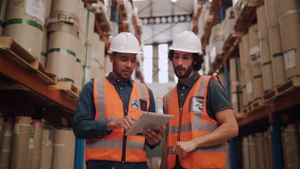 Zwei lächelnde junge männliche Arbeiter in Uniform, nachdem sie sich im Industrielager die Hand gegeben haben, schauen auf das digitale Tablet — Stockvideo