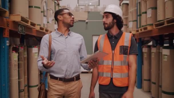 Různorodý dozorce a tovární dělník, kteří diskutují a kontrolují výrobky ve velkém skladu pomocí digitálního tabletu — Stock video