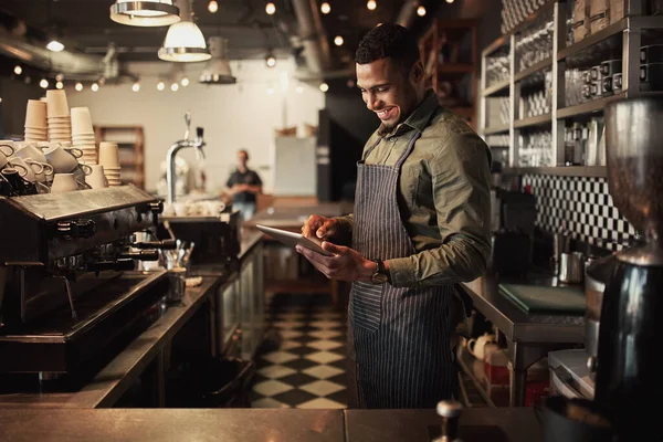 Vrolijke jonge afro-Amerikaanse cafe eigenaar draagt zwart gestreepte schort met behulp van digitale tablet — Stockfoto