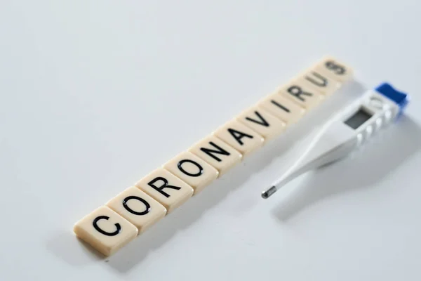 Коронавирус написан с черепицей и термометром на белом фоне. — стоковое фото