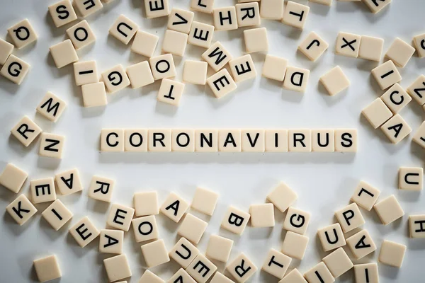 Coronavirus spelt on scrabble tiles surrounded by other tiles in the centre — 스톡 사진