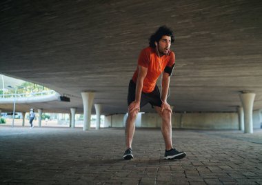 Spor kıyafetli çekici genç adam nefes nefese köprünün altında antrenman yaptıktan sonra mola veriyor. Yeni yılda koşan adam.