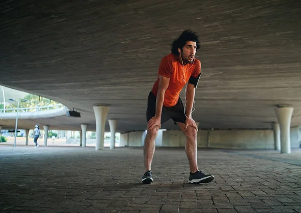 Atractivo joven deportivo en corredor de ropa deportiva respirando jadeando y tomando un descanso después de correr entrenamiento bajo el puente - hombre corriendo en el nuevo año —  Fotos de Stock