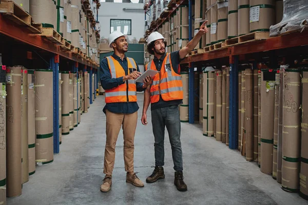 Volledige lengte van vreugdevolle professionele managers die samenwerken terwijl ze in het magazijn digitale tablet vasthouden die wijst naar kartonnen doos op de plank — Stockfoto