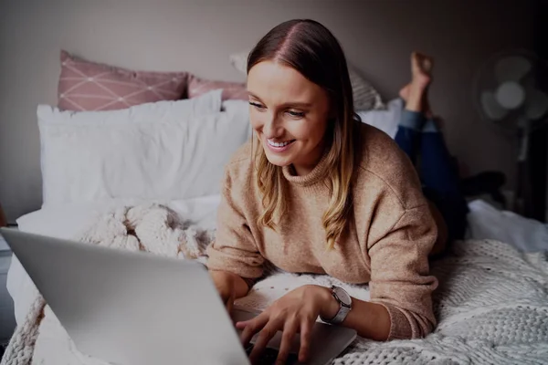 Portret van een glimlachende casual jonge vrouw die thuis aan haar laptop werkt tijdens de covid-19 quarantaine die zelfisolatie verzekert — Stockfoto