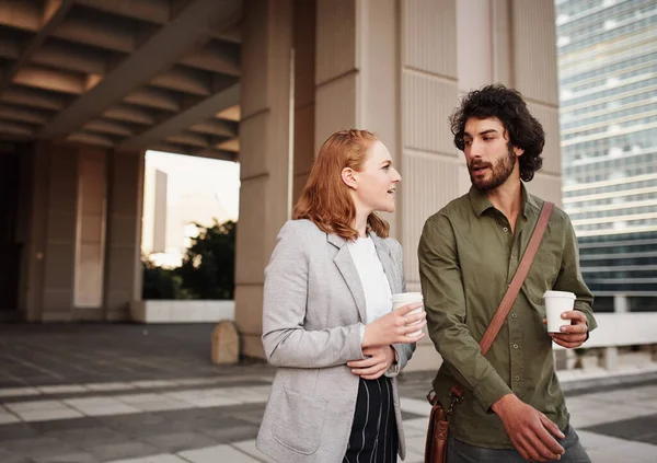 Mannelijke en vrouwelijke zakenpartners drinken koffie in een gesprek buiten tijdens het lopen van het gebouw — Stockfoto