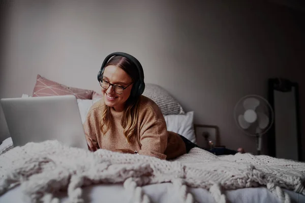 Jonge vrouw met een bril in een koptelefoon die naar muziek luistert en online lessen volgt - jonge student op een online videogesprek — Stockfoto
