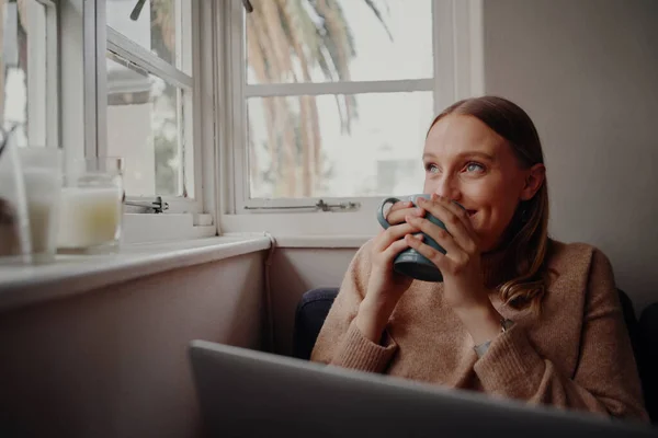 Zelf geïsoleerde jonge vrouw glimlachend genieten van het werk van thuis uit het drinken van koffie en dagdromen — Stockfoto