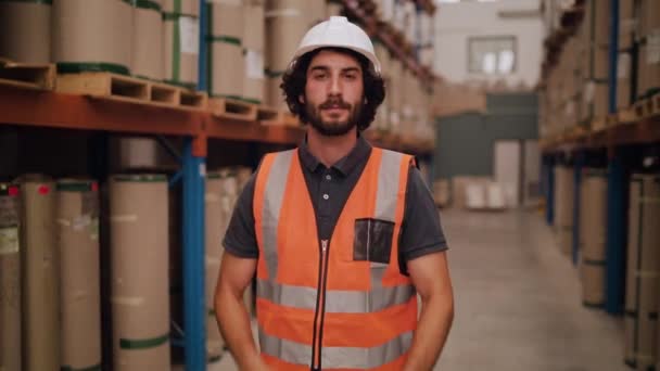 Уверенный молодой мастер или надзиратель склада, стоящий среди строительных материалов и смотрящий в камеру — стоковое видео