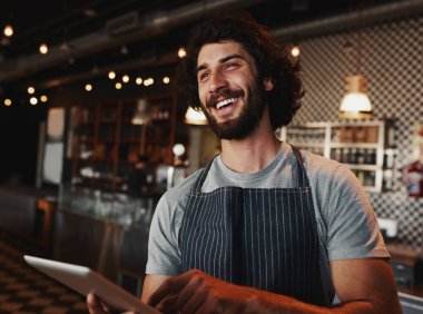 Kafkasyalı yakışıklı kahve dükkanı sahibi elinde dijital tabletle gülüyor.
