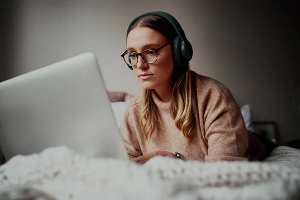 隔離中に自宅でオンラインビデオ通話でヘッドフォンを着用する眼鏡をかけた若い女性-オンラインクラスの講義に出席する若い女性学生-音楽を聴く — ストック写真