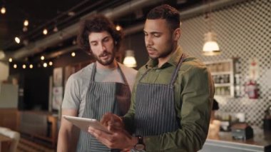 Tablete bakıp, bir kafenin işletme sahiplerinin işlerini geliştirmek için teknolojiyi kullanmalarını tartışan iki etnik çeşitlilikte genç kafe sahibi.