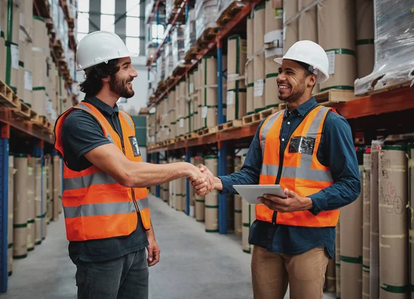 Two cheerful man making a firm handshake in logistics workhouse holding a digital tablet in safety helmet and vest — Stock Photo, Image