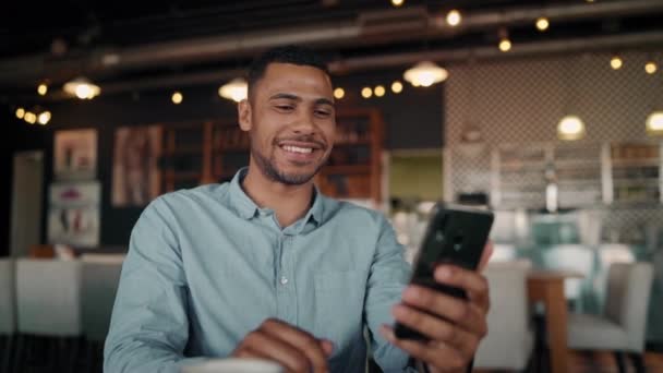 Młody człowiek śmieje się podczas rozmowy z przyjacielem za pomocą smartfona z technologii wideodomofonu w kawiarni — Wideo stockowe