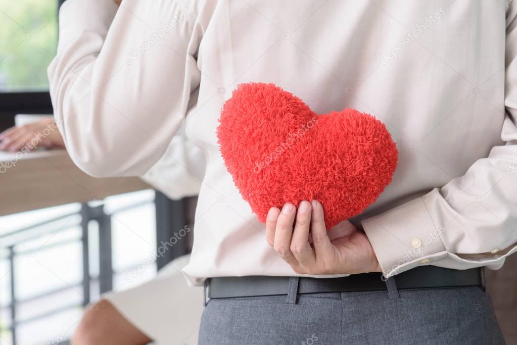 Man holding red heart behind his back to surprise woman