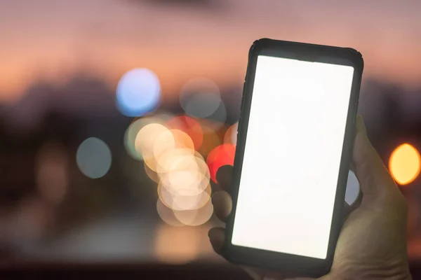 Smartphone in der Hand auf einem Hintergrund mit Bokeh und Unschärfe — Stockfoto