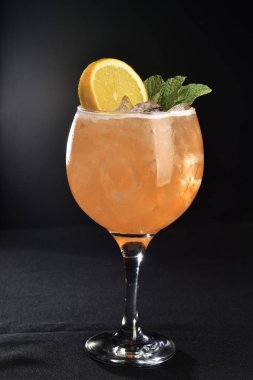Siyah arka planda turuncu parçalı cam bardakta meyve suyu.