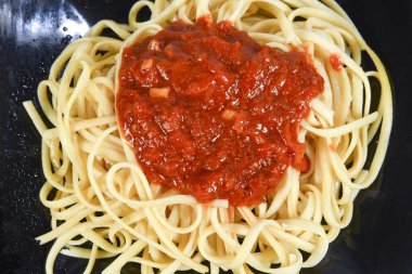 Beyaz arka planda izole edilmiş siyah tabakta zeytinyağlı bolonez soslu bir tabak spagetti.