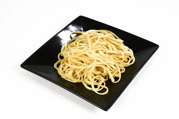 白い背景の上に黒いプレートの上にオリーブオイルと新鮮なスパゲティのプレート — ストック写真