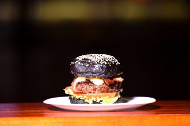 Lezzetli el yapımı hamburger sandviçi, siyah arka planda bir taşın üzerinde servis edilen siyah soğanlı marul ve ekmek.