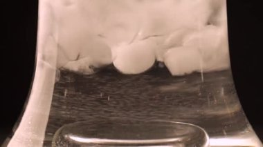 Buz düşer ve siyah bir zeminde suda döner. Su ve buzlu nargile şişesi.