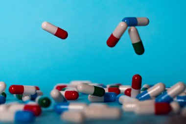 Renkli haplar mavi arka plana düşer. İlaçlar düşüyor. Mavi masadaki kırmızı, yeşil, mavi ve beyaz haplar.