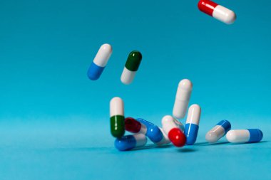 Renkli haplar mavi arka plana düşer. İlaçlar düşüyor. Mavi masadaki kırmızı, yeşil, mavi ve beyaz haplar.