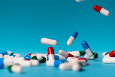 Renkli haplar mavi arka plana düşer. İlaçlar düşüyor. Mavi masadaki kırmızı, yeşil, mavi ve beyaz haplar.
